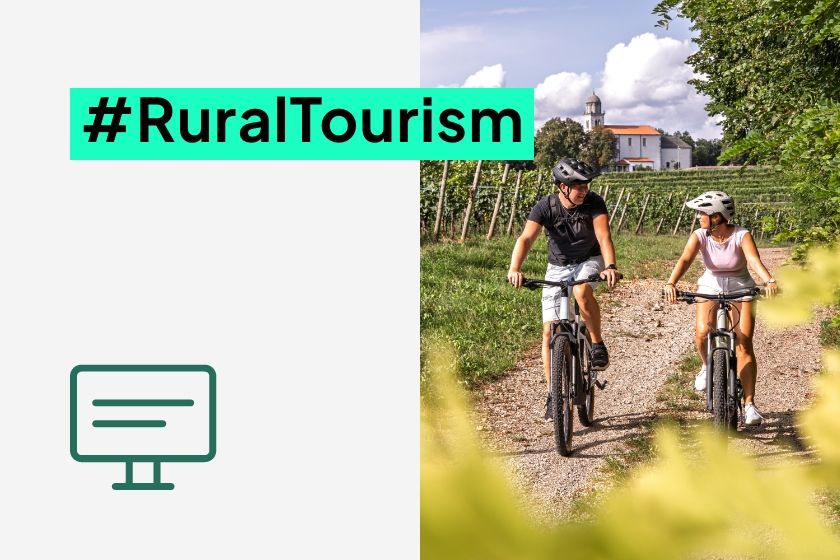 Two cyclists on mountain bikes riding through a vineyard path with a church in the background, next to the hashtag #RuralTourism.