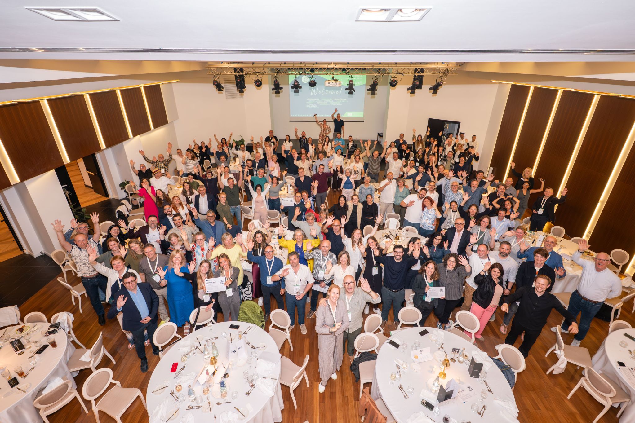 big group of people in a conference room photographed from above, they have their hands in the air