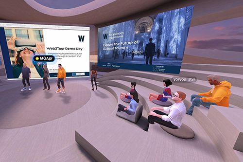 A virtual reality auditorium with seated and standing avatars facing two large presentation screens during a Web3‑themed event.